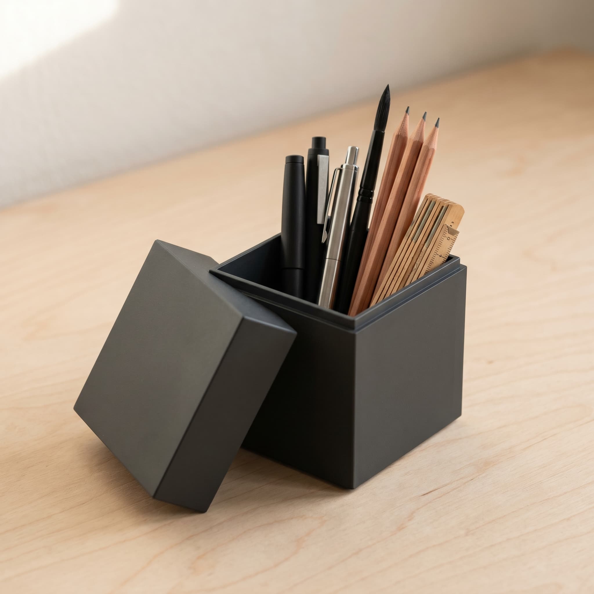 Charcoal cube box repurposed as desk storage, holding pens and small brushes