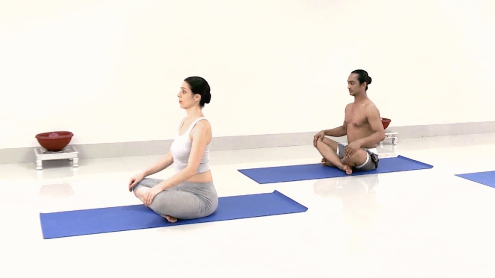 A grounding seated practice — two practitioners sitting cross-legged on mats.